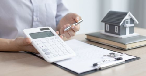 Man zit aan bureau met miniatuurhuis en rekenmachine